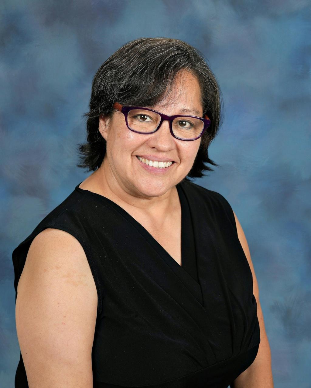 Lady with black hair, wearing a black top with black glasses